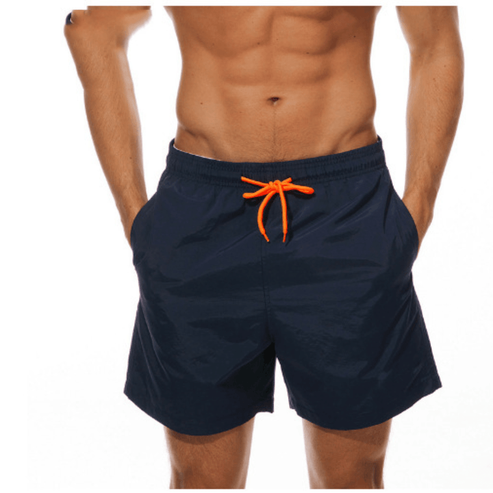 Short de bain bleu marine vu de face sur un mannequin, cordon orange noué, mains dans les poches. 7