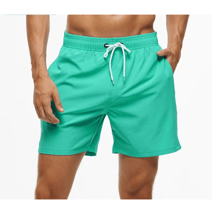 Short de bain vert menthe porté, ceinture élastique à œillets et cordon blanc, une main dans la poche. 8