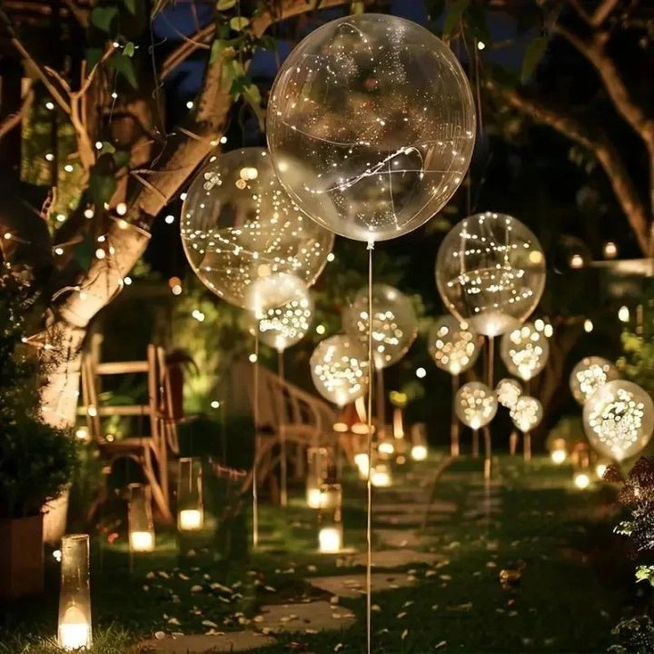 Ballons lumineux de différentes tailles flottant dans un jardin nocturne, avec bougies posées au sol le long d'un chemin. 5