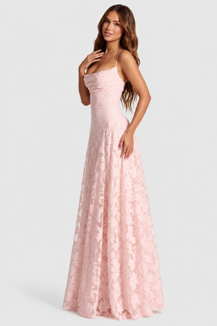 Robe rose pâle en dentelle florale, encolure drapée et fines bretelles, portée par une mannequin vue de trois quarts, main sur la poitrine. 1