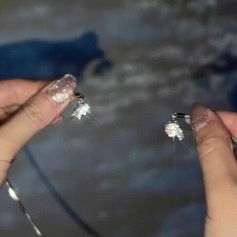 Deux mains aux ongles pailletés tiennent chacune une moitié du cœur scintillant, prêtes à les rapprocher pour fermer le collier. 1