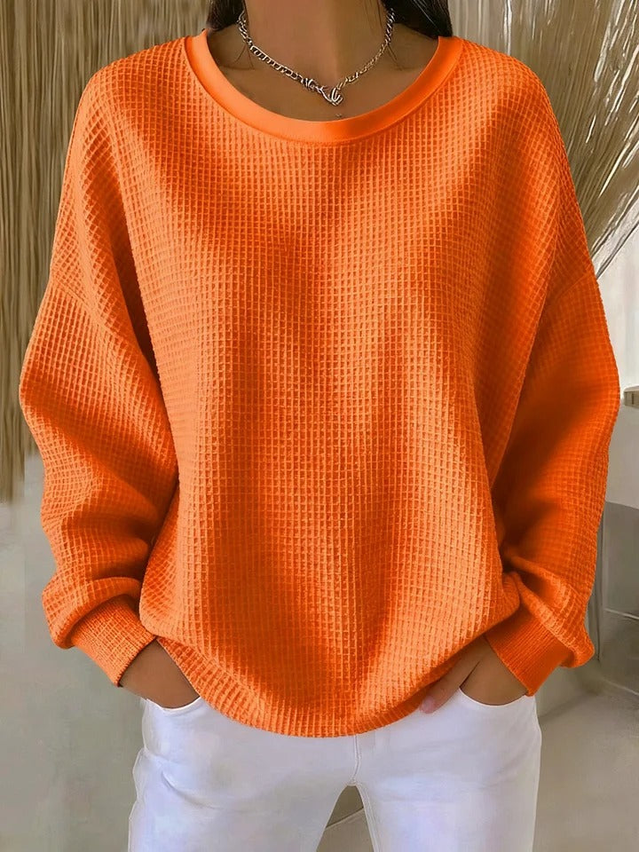 Pull gaufré orange vif à col rond et manches amples, porté avec un pantalon blanc et un collier argenté. 8