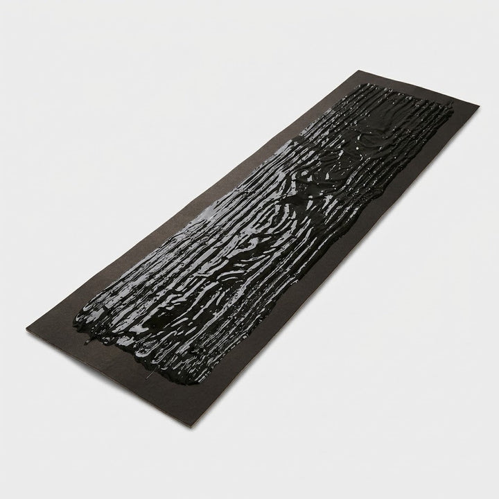 Plaque rectangulaire en carton noir enduite de colle brillante, vue en biais sur fond blanc 6