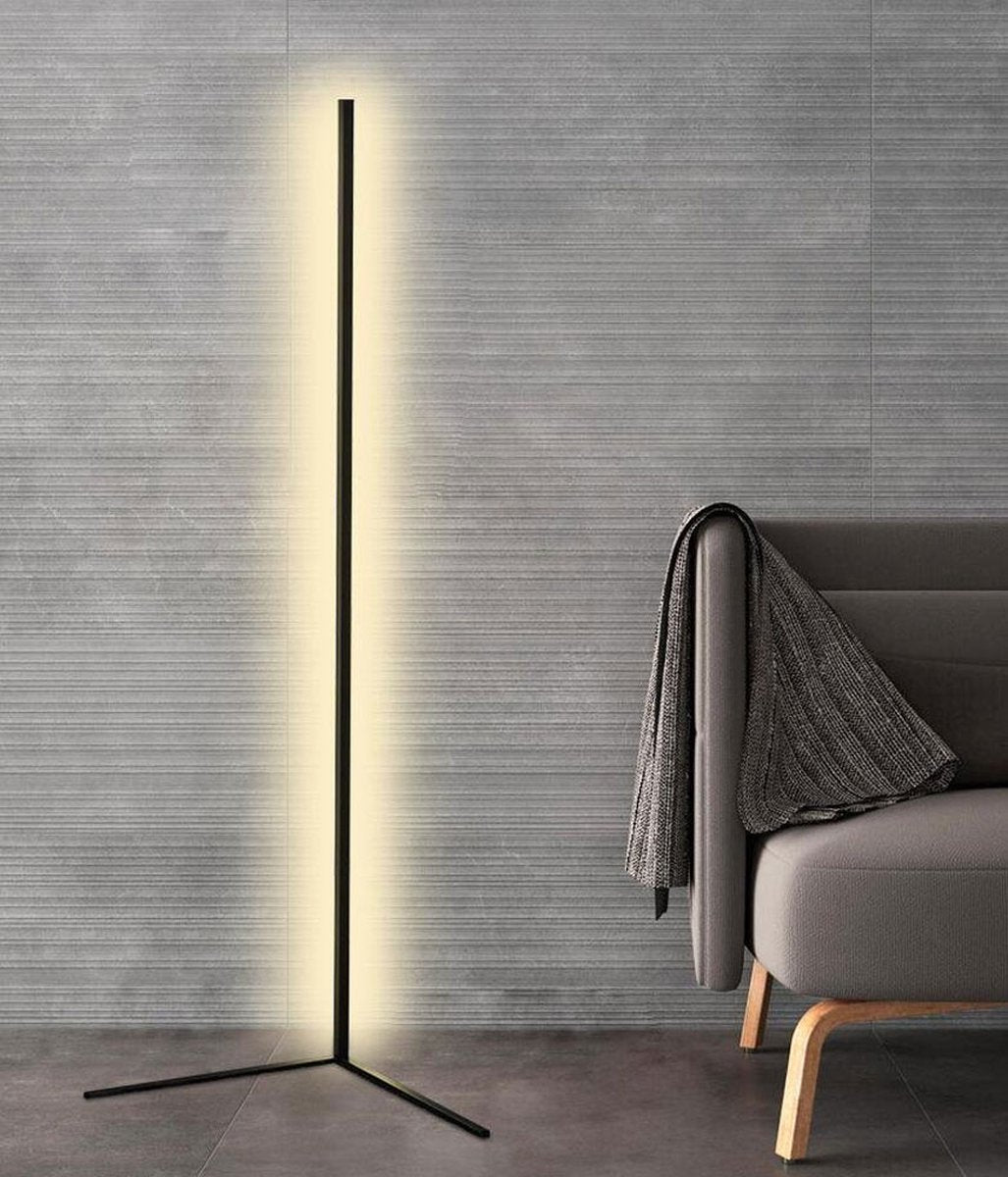 Lampadaire noir à pied en V, lumière blanc chaud, devant un mur gris strié et un fauteuil avec plaid 8