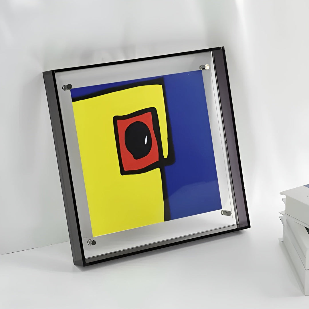 Cadre acrylique à bords noirs posé en biais contre un mur blanc, avec une illustration abstraite jaune, bleue et rouge. 6