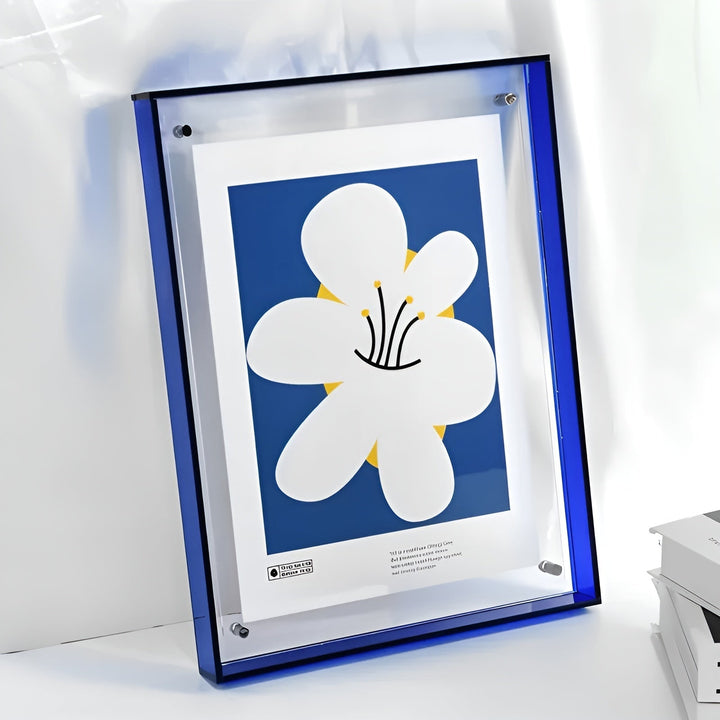 Cadre acrylique à bords bleu foncé appuyé contre un mur, avec une affiche d'une grande fleur blanche sur fond bleu. 14