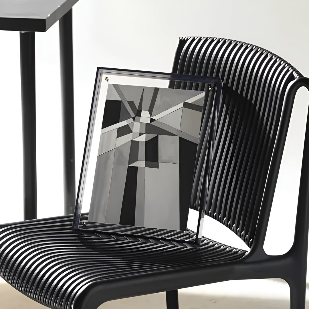 Cadre acrylique sombre posé sur une chaise noire à lattes, présentant un motif graphique géométrique en noir et gris. 7