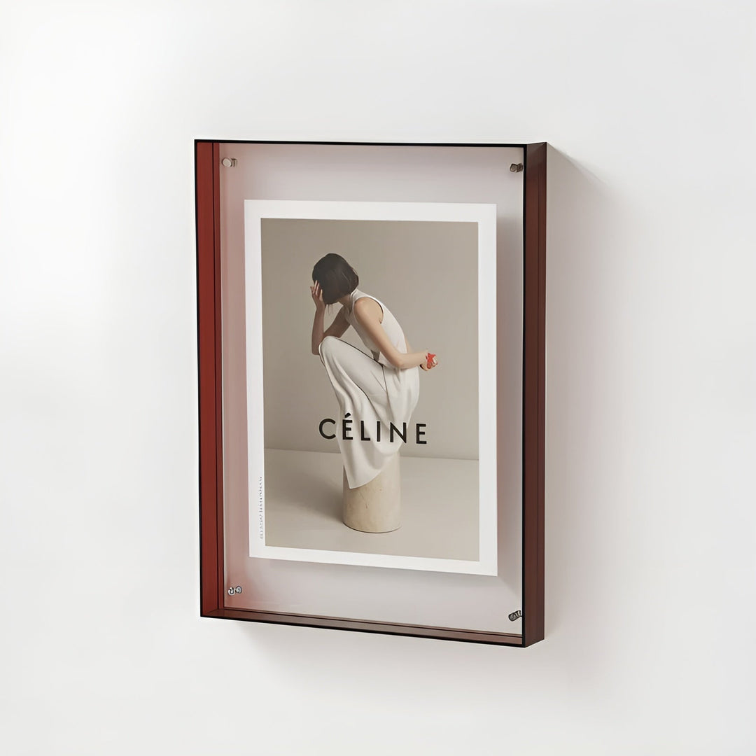 Cadre acrylique à bords brun rouge accroché au mur, contenant une photo de mode d'une femme en robe blanche accroupie sur un socle. 20