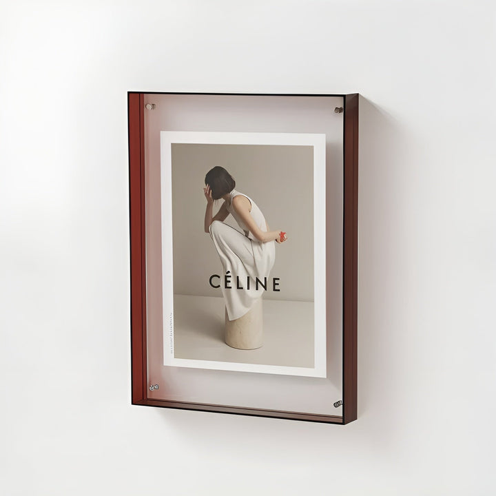 Cadre acrylique à bords brun rouge accroché au mur, contenant une photo de mode d'une femme en robe blanche accroupie sur un socle. 20
