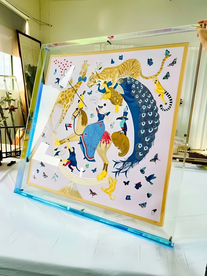 Grand cadre acrylique transparent à bord bleu clair, tenu en biais, contenant un foulard imprimé d'animaux, de papillons et d'un paon. 17