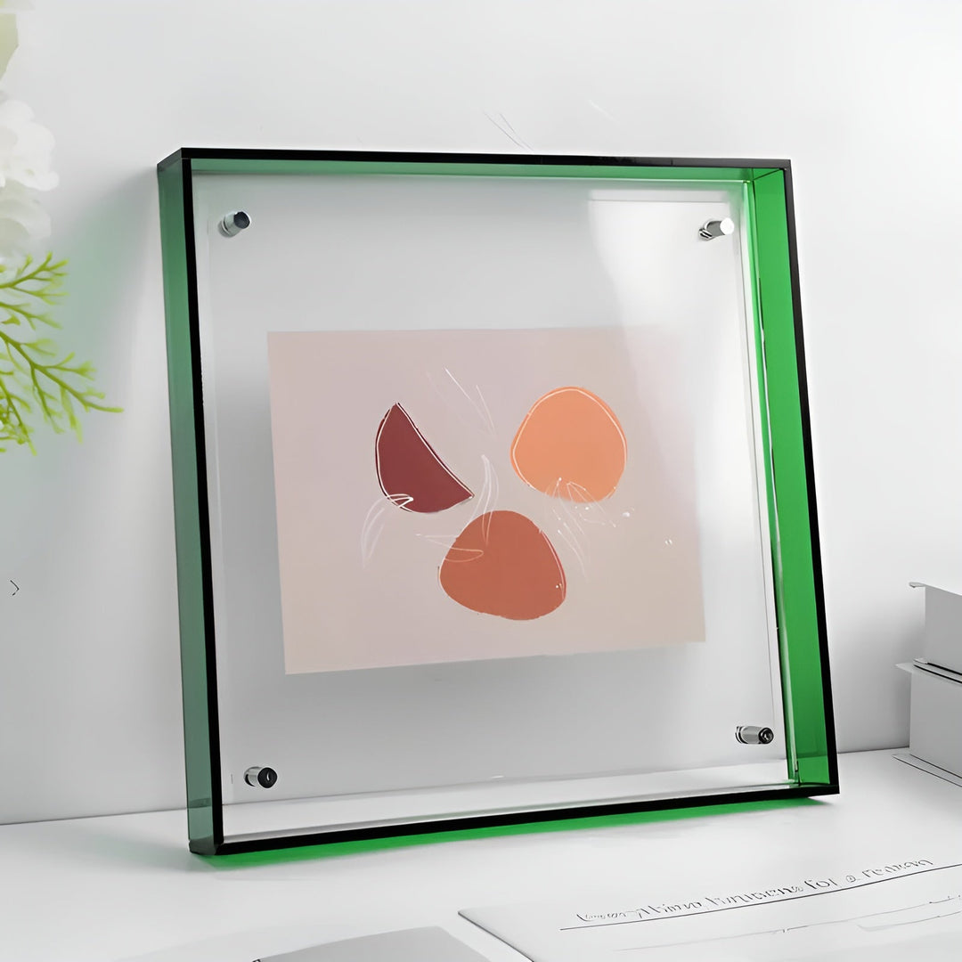 Cadre acrylique transparent à bordure verte posé sur un bureau, avec quatre fixations métalliques et une illustration abstraite orangée à l'intérieur. 21