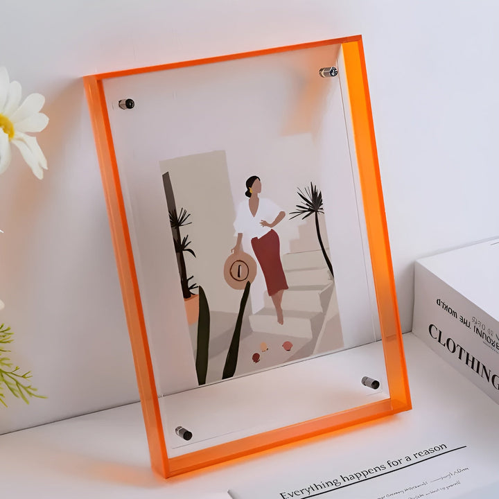 Cadre acrylique à bords orange vif sur une étagère, avec une illustration de femme à chapeau près de palmiers, à côté d'une fleur blanche. 10