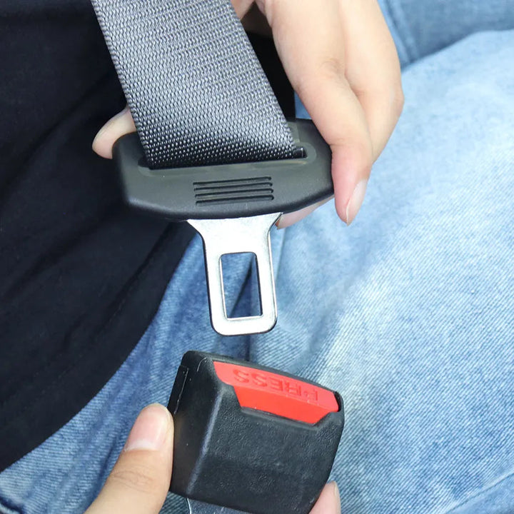 Mains approchant la languette métallique de la ceinture d'un insert noir à bouton rouge, sur un jean 4