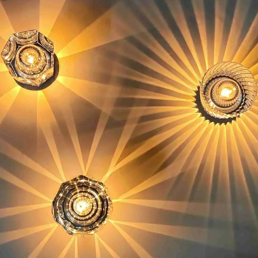 Vue de dessus de trois lampes en cristal allumées, aux formes hexagonale, ronde et à facettes, diffusant des rayons dorés. 2