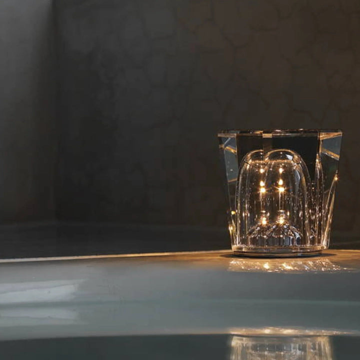Lampe en cristal facetté allumée posée sur un rebord sombre, avec une petite cloche de verre lumineuse en son centre. 4