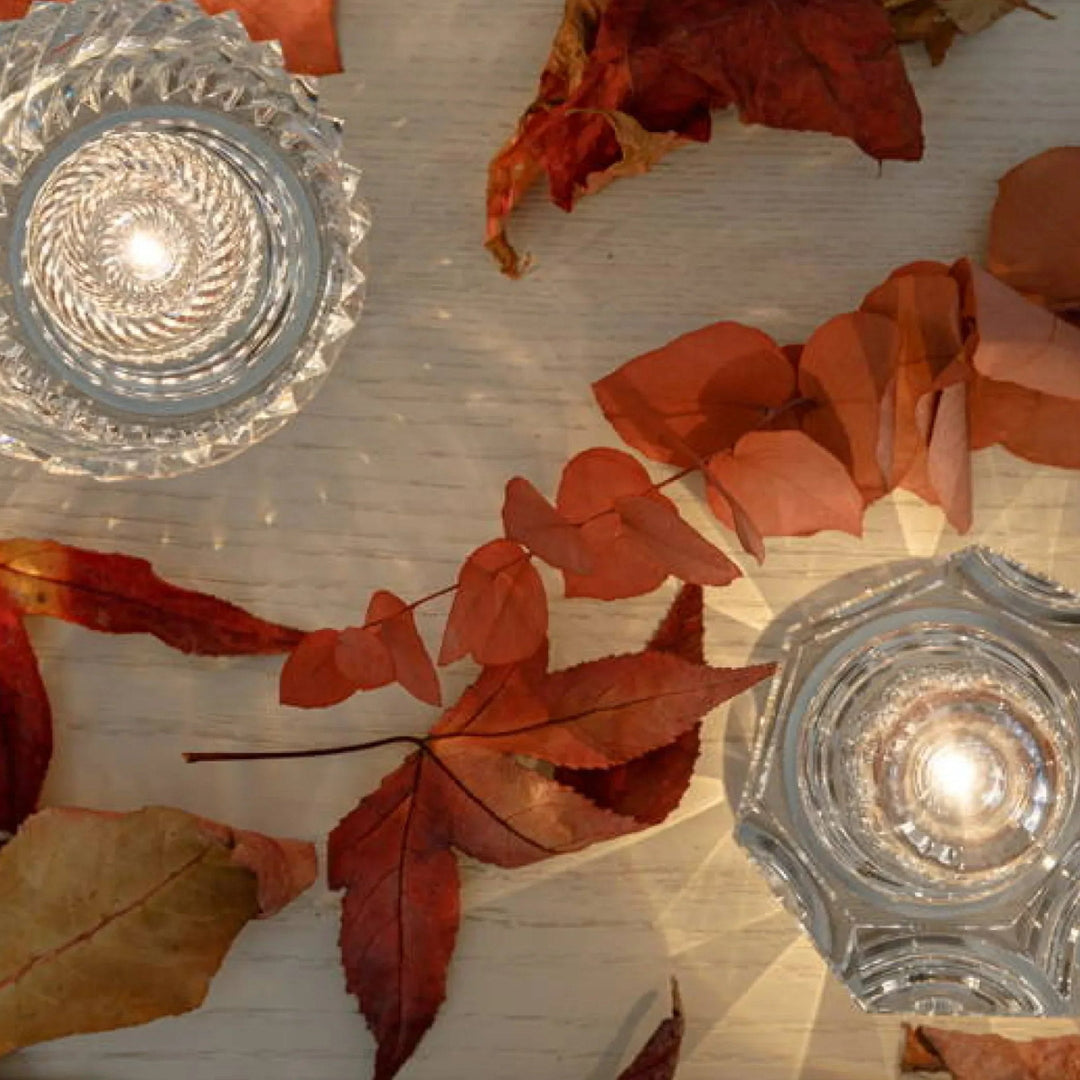 Vue de dessus de deux lampes en cristal allumées entre des feuilles d'automne rouges sur une table en bois clair. 10