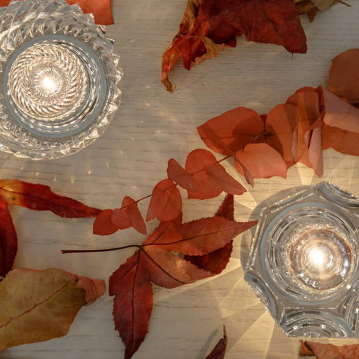 Vue de dessus de deux lampes en cristal allumées entre des feuilles d'automne rouges sur une table en bois clair. 10