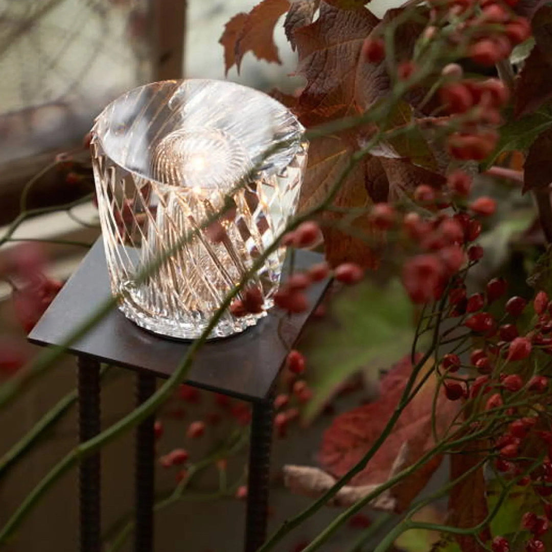 Lampe en cristal à motif en losanges allumée sur un petit support métallique, entourée de branches de baies rouges. 11