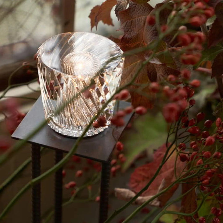 Lampe en cristal à motif en losanges allumée sur un petit support métallique, entourée de branches de baies rouges. 11