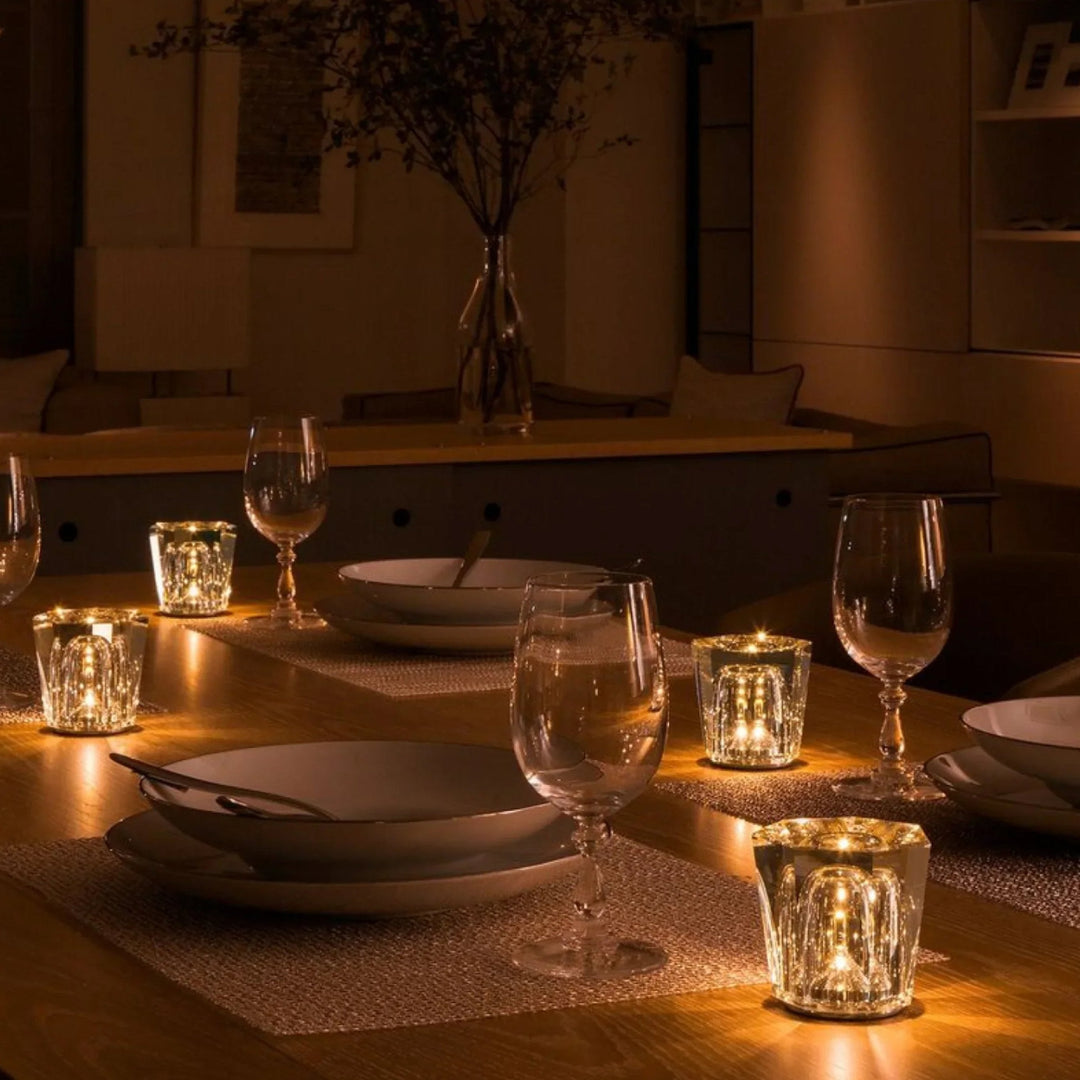 Table de repas dressée avec quatre petites lampes en cristal allumées entre les assiettes et les verres à pied, ambiance tamisée. 9