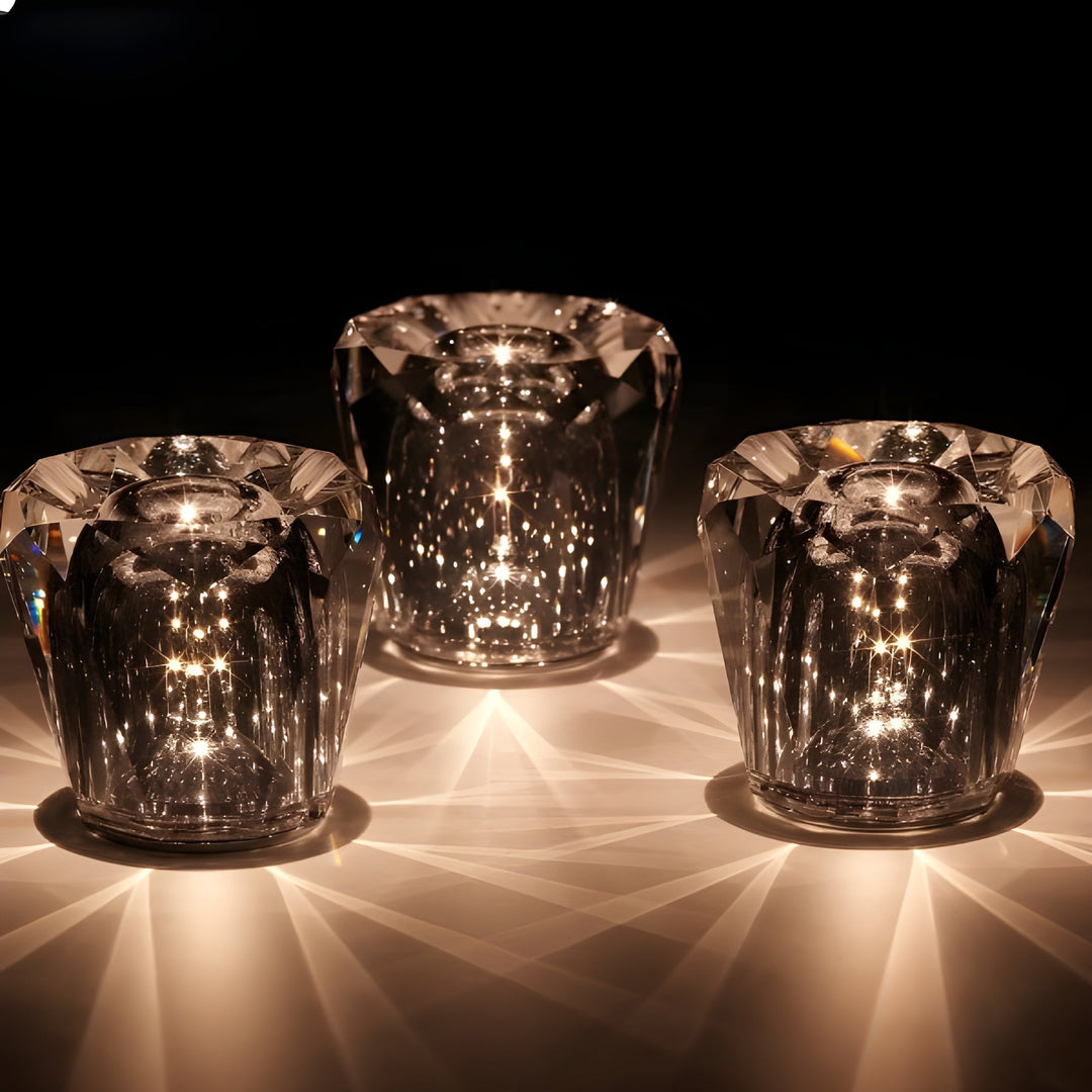 Trois lampes en cristal taillé en diamant allumées sur fond noir, avec rayons de lumière chaude étalés sur la table. 16