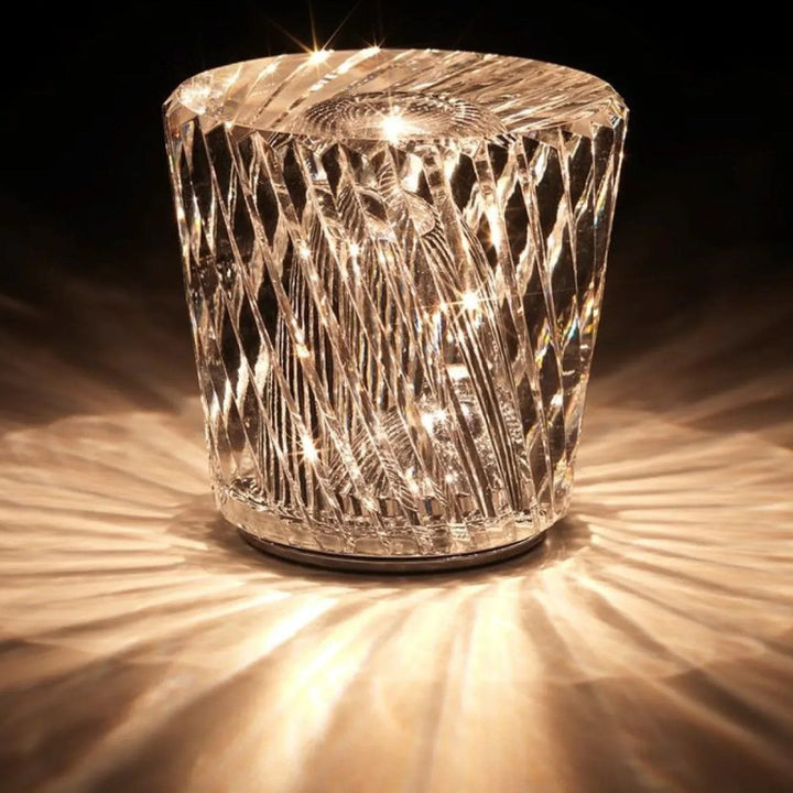Lampe en cristal à facettes en losanges allumée sur fond sombre, projetant des rayons de lumière dorée tout autour. 13