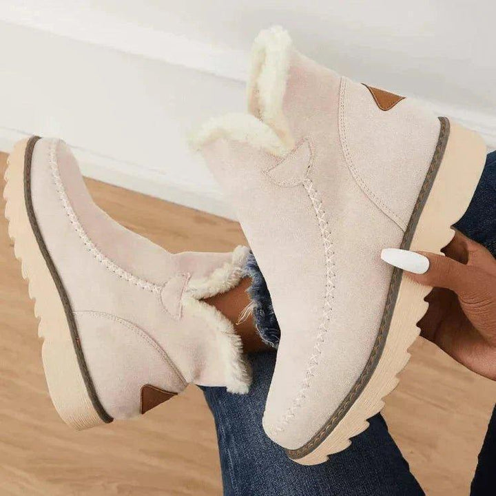 Bottines beige tenues à la main, jambes croisées, en gros plan sur la doublure duveteuse, les surpiqûres et la semelle crantée. 6