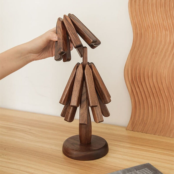 Une main retire les dessous de plat pliants empilés sur leur support en bois en forme de petit arbre. 1