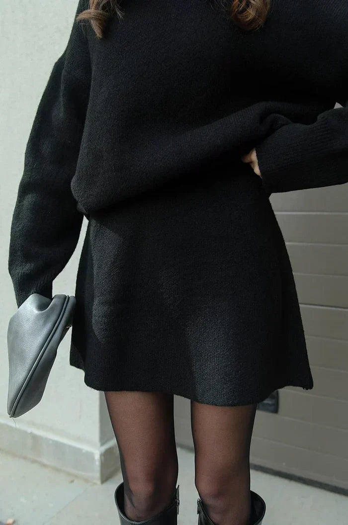 Détail de la jupe noire courte et évasée en maille, portée avec le pull noir, collants et bottes noires. 7