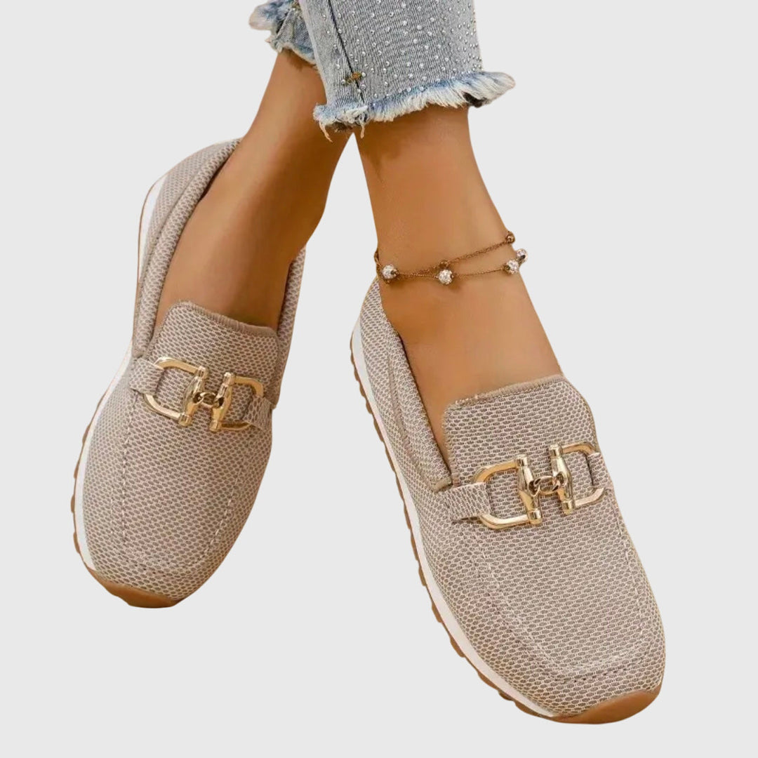 Mocassins beiges portés, pieds croisés, avec détail de la boucle dorée et de la maille 10