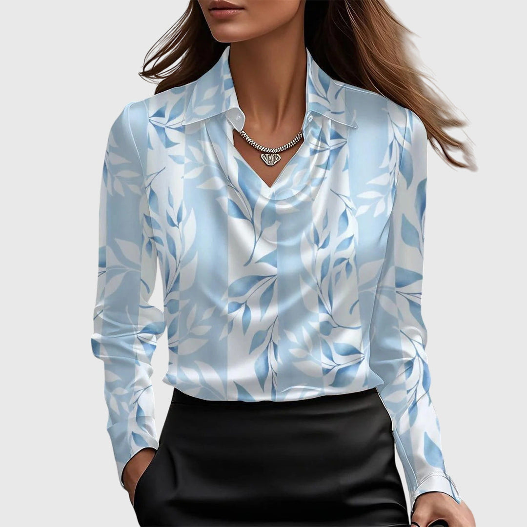 Blouse en satin à motif de feuillages bleu clair sur fond blanc, col drapé, portée avec une jupe noire. 5