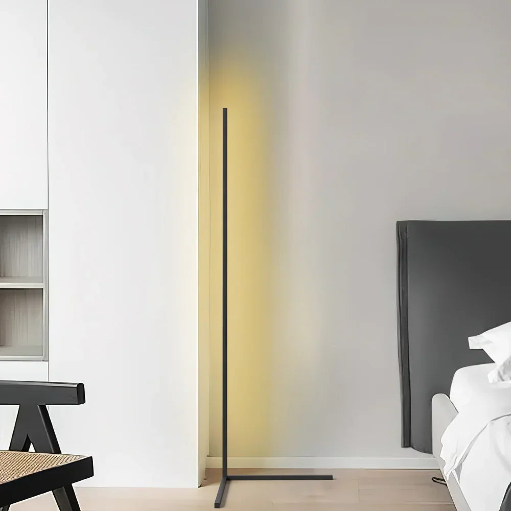 Lampadaire noir en forme de L éclairé dans une pièce blanche, avec chaise en bois et lit 7