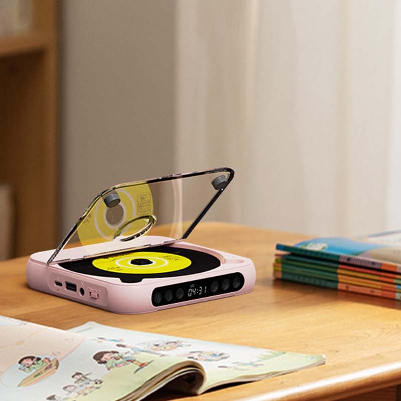 Lecteur rose couvercle ouvert sur une table en bois, avec un livre d'images ouvert au premier plan et une pile de livres derrière. 10