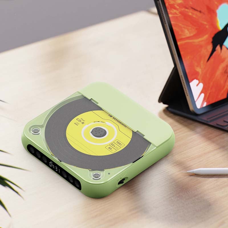 Lecteur vert fermé avec disque jaune visible sous le couvercle, posé sur un bureau à côté d'une tablette et d'un stylet. 12