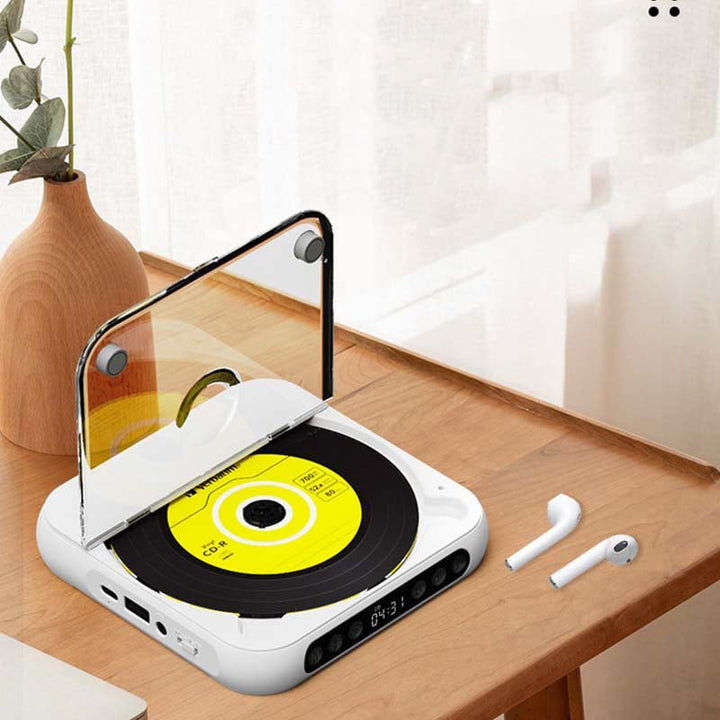 Lecteur blanc ouvert posé sur un bureau en bois, avec disque jaune visible, deux écouteurs sans fil et un vase à côté. 8