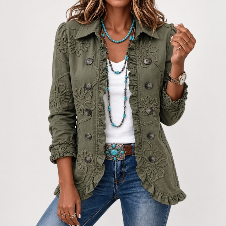 Buste d'une femme sur fond clair, veste kaki à fleurs brodées et volants portée ouverte, avec longs colliers turquoise et boucle de ceinture. 4
