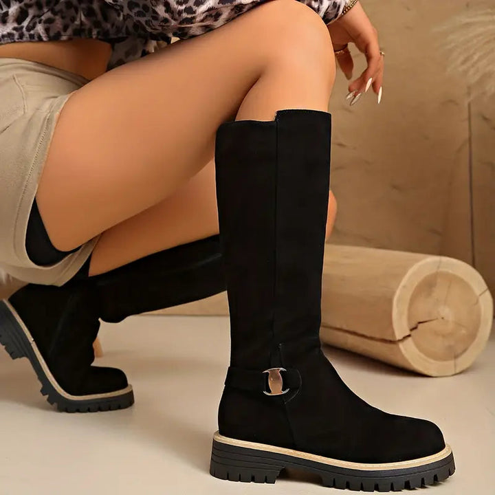 Femme accroupie en short portant des bottes noires hautes à semelle épaisse, avec boucle dorée sur le côté. 4