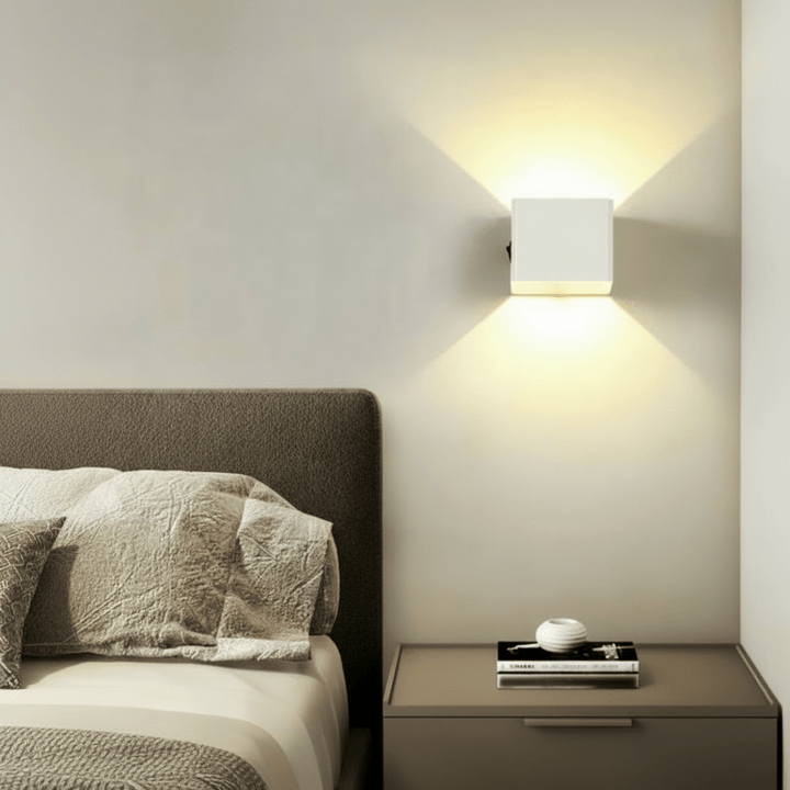 Applique cubique blanche allumée au-dessus d'une table de chevet, en tête de lit, diffusant une lumière chaude dans une chambre. 3