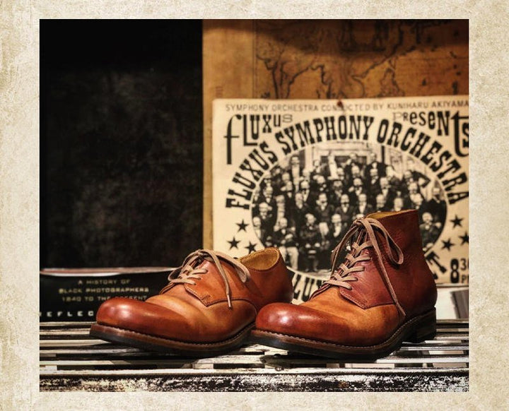 Bottines en cuir brun cognac posées sur une étagère en bois, dans un décor d'ambiance vintage avec affiche et carte. 3
