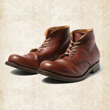 Paire de bottines en cuir brun cognac à lacets, vue trois quarts avant sur fond beige texturé. 1