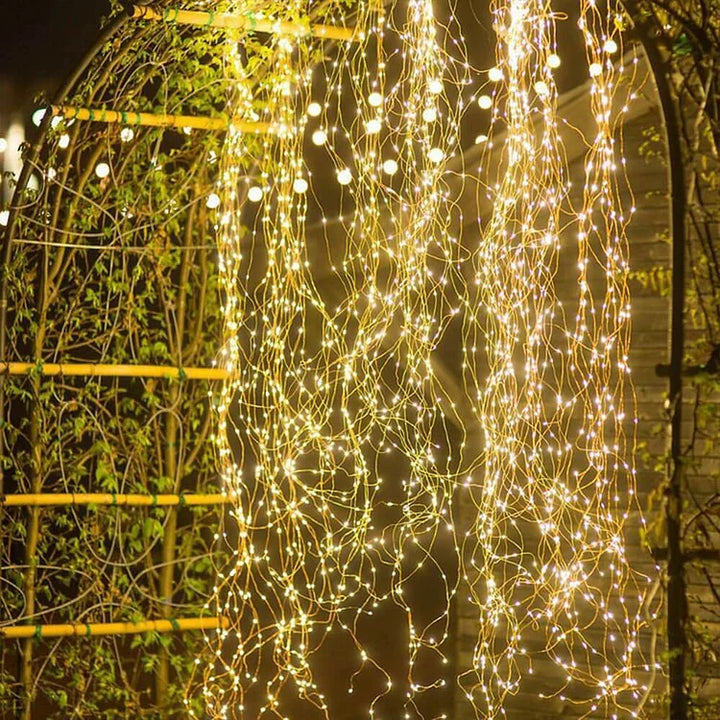 Cascades de fils lumineux dorés retombant le long d'une arche de jardin, aux petites lumières scintillantes de nuit. 5