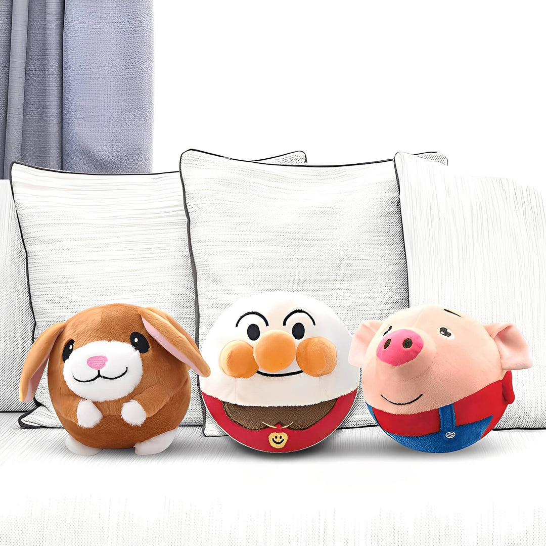 Trois balles en peluche, un lapin brun, un personnage blanc à nez orange et un cochon rose, posées devant des coussins. 1