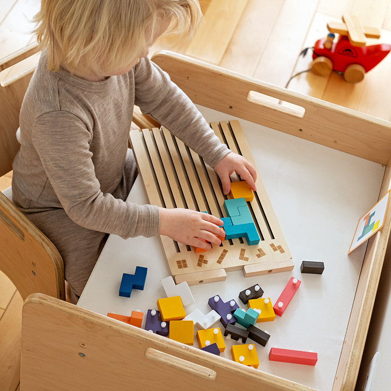 Enfant assis à une table en bois qui place des pièces sur le plateau, les autres pièces à picots étalées devant lui. 8