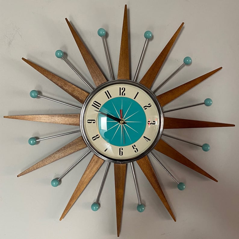 Vue de face de l'horloge étoile au mur, cadran turquoise et crème bordé de chrome, chiffres noirs et trotteuse rouge. 4