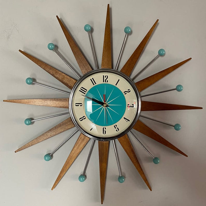Vue de face de l'horloge étoile au mur, cadran turquoise et crème bordé de chrome, chiffres noirs et trotteuse rouge. 4