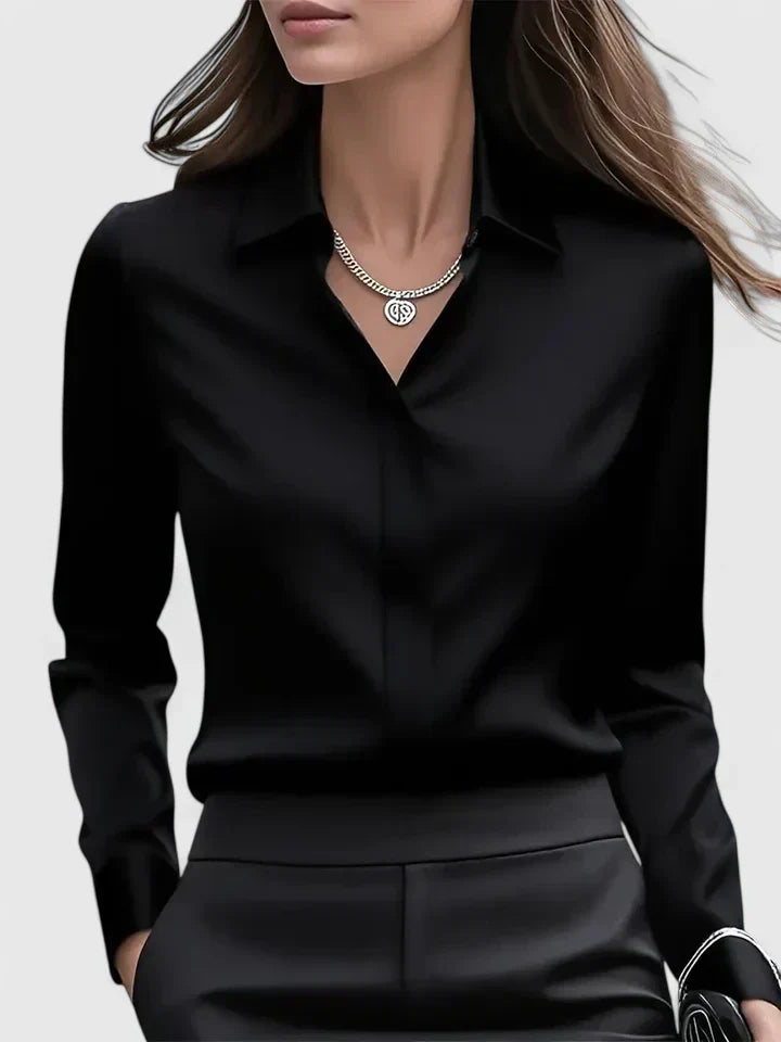 Vue de face du chemisier noir fluide à col ouvert, porté avec un pantalon noir et un collier. 3