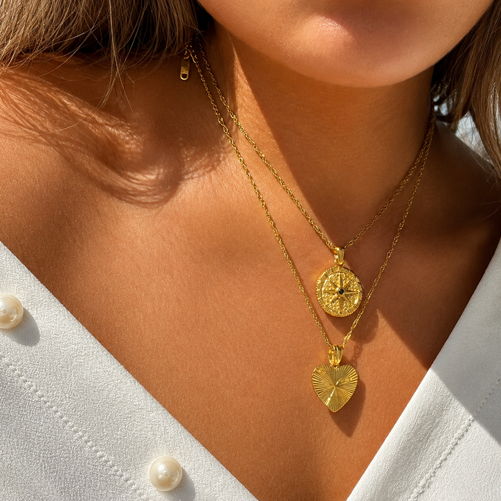 Collier porté au cou par une femme en chemisier blanc, superposé à un second collier à pendentif cœur strié doré. 3