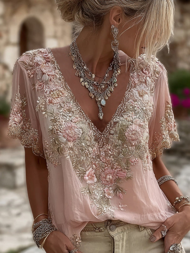 Femme portant la blouse rose pâle, vue de face en gros plan sur le décolleté en V brodé de fleurs et de perles, avec colliers argentés. 1