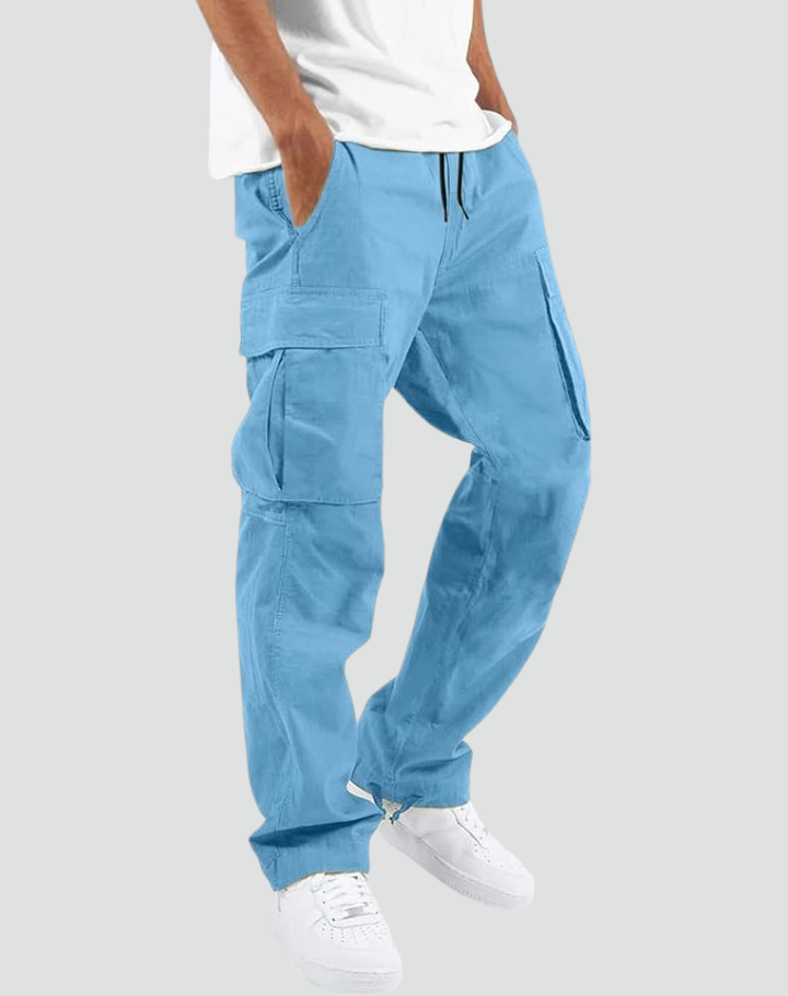 Pantalon cargo bleu ciel porté par un modèle avec t-shirt blanc et baskets blanches, sur fond gris clair. 14