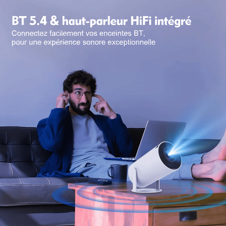 Homme assis sur un canapé se bouchant les oreilles, ordinateur portable et projecteur allumé sur la table basse 9